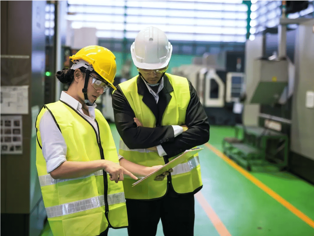 Two workers in safety gear with clipboard at industrial facility.