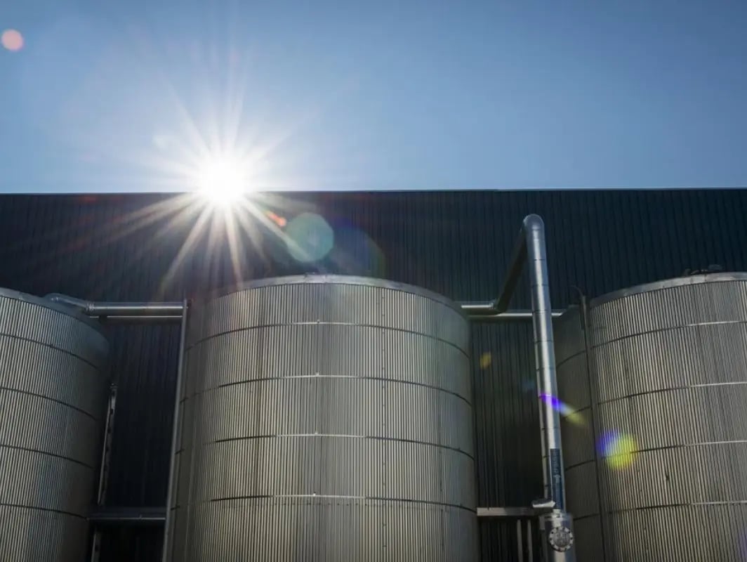 Sun shining brightly above industrial silos with lens flare effect.