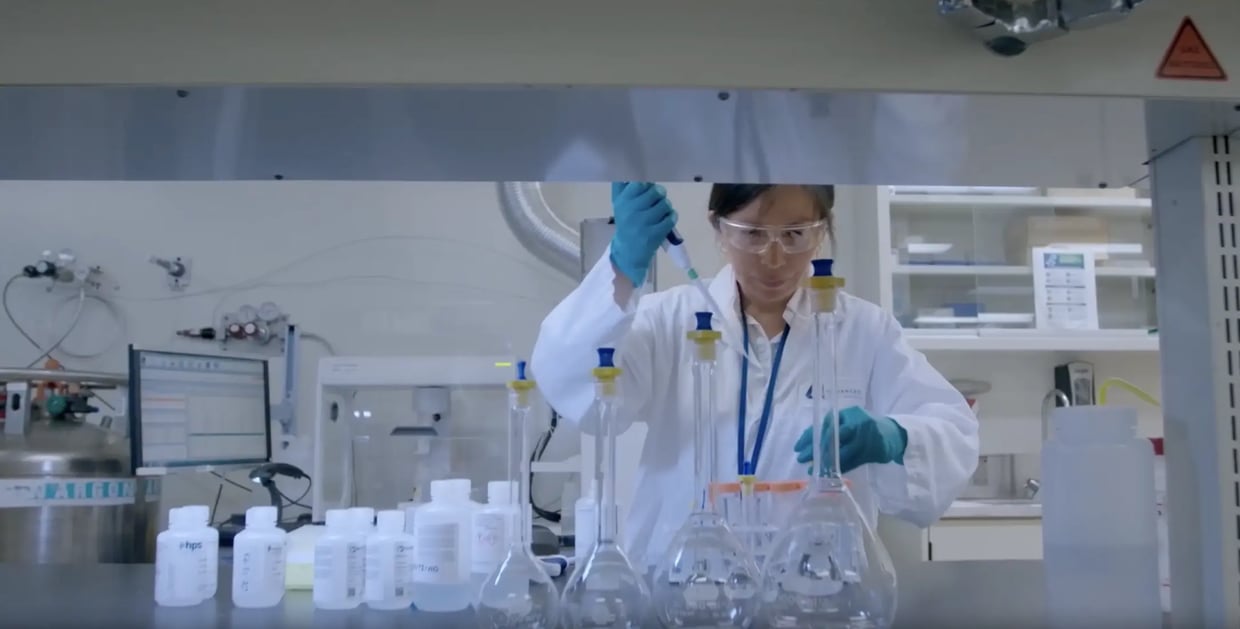 Scientist using a pipette with lab flasks and bottles on a bench in a laboratory.